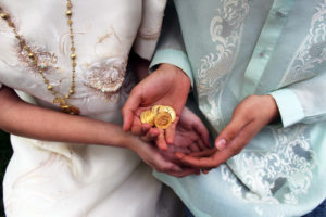 Closeup of a couples' hands exchanging coins in Philippine wedding attire