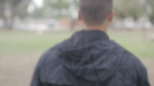 Blurred image of man in striped gray hoodie near green field