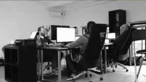 Four people sitting in an office on desktop computers