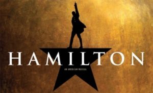 "Hamilton: An American Musical." Silhouette of a man in 18th century dress reaching a hand to the sky, standing on a star. Gold background.