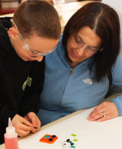 An adult helps a child create a fused glass magnet during the Summer Antique and Food Market