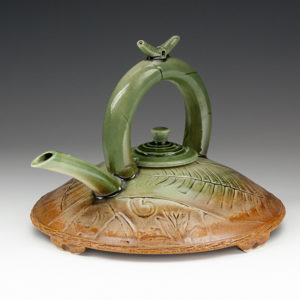 Wide, flat teapot painted tawny to green from bottom to top with a small lid, large handle, and spout. Created by Stephen Fabrico.