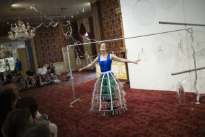 Martha McDonald dancing in a hoop skirt decorated with hanging test tubes around each tier during "Phantom Frequencies" in the Museum of American Glass