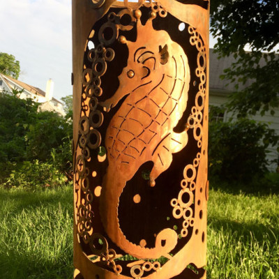 A cylindrical metal garden sculpture with a seahorse surrounded by bubbles cut into the sides. Created by Sandra Webberking.