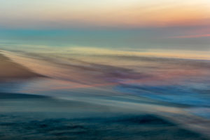 Photograph by Frederick Ballet of an ocean with deep blues and highlights of pink and yellow, blending seamlessly with the sky