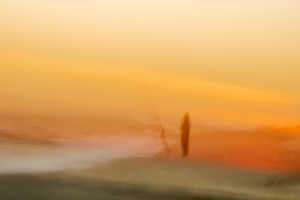 Photograph by Frederick Ballet of a shifting silhouette of a person and fishing rod right on the edge of the ocean's tide in an orange sunset