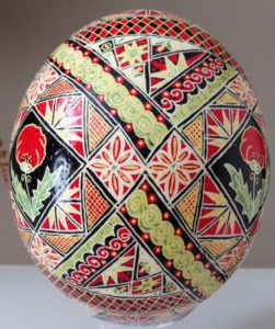 Pysanky by Marino Diaz full of flower, poppy, and triangle motifs in green, red, yellow, and black