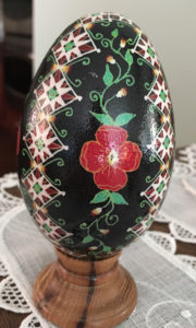 A pysanky by Marino Diaz. The egg is black with green vines and a red flower in the center and diamond patterns surrounding.