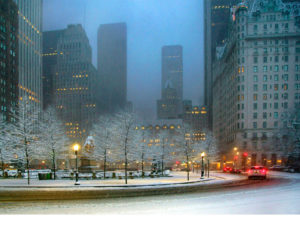 Photograph by Michael Leu of a city scene dusted in white snow, highlighted by the yellow lights from the lampposts and the bright red tail lights of passing cars