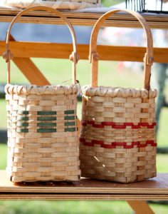 Two woven baskets by Mary May on a bench, one with green accents woven through and one with two red stripes woven through.