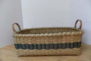 A long woven basket by Mary May with a large deep blue stripe woven around near the bottom