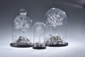 Three flameworked clear glass trees of various sizes by Stephen Brucker with exposed roots, each contained under a glass cloche