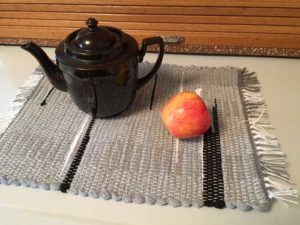 A teapot and apple sit on top of a grey handwoven placemat by Belinda DeCicco