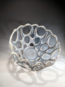 White and light blue decorative bowl by Erika Novak and Drew Darley with large oval holes of various sizes.