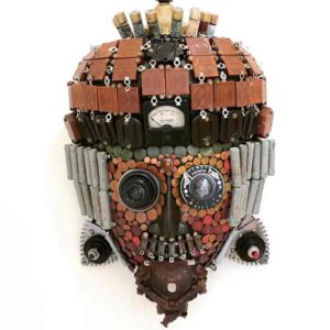 A found object mask by Larry Agnello, referencing masks from Africa. Red, yellow, and brown tiles fill its head and its chin is made with a small coocoo clock.