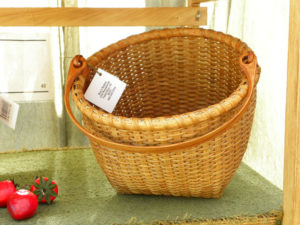 A large woven basket by Mary May with a large wooden handle.