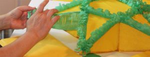 A pair of hands works on a Phillipine parol, an ornamental lantern shaped like a yellow star with green borders.