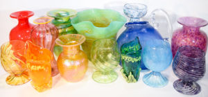 A collection of glass vases in a spectrum of colors from red to violet.