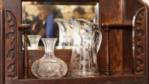 Two clear glass vessels sitting on an antique wooden shelf with a mirror behind them.