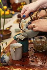 Closeup of hands carefully pouring tea from a small teapot into a cup