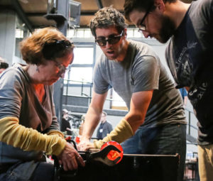 A small group of glassblowers work together to shape a molten piece of glass.