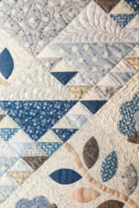 Detail of a quilt with patches of patterned fabric in soft tones blues of browns.