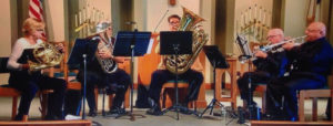 Ceremonial brass band of 5 people playing indoors.