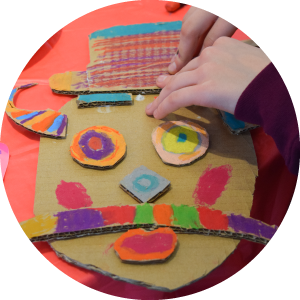 Child creating a colorful cardboard mask with a hat and mustash.