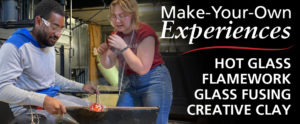 A long digital banner for "Make-Your-Own- Experiences" This is in large white text at the top right over a dark vignette. Below that is a red wavy line and under that is: "HOT GLASS", "FLAMEWORK", "GLASS FUSING", and "CREATIVE CLAY" To the left is studio resident aritst, Kendall Frank, teaching a man how to work with glass. He is sitting on a bend on the left with a metal rod that has a glass ball on the end, in his left hands. His right hand is holding a metal spoon-like tool to shape the glass. He is wearing a grey and blue sweatshirt and has clear safety goggles on. Kendall on the right is wearing a red t-shirt and blue jeans, and is wearing clear glasses.