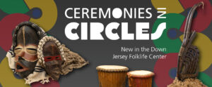 Image of a banner for the "Ceremonies in Circles" exhibit. In the center of the banner is large white text that reads "Ceremonies in Circles" above "New in the Down Jersey Folklife Center" on a dark gray background. Below this white text is the top of two pieces from the Ceremonies in Circles exhibit. The two tall drums are wide at the ends and thin in the middles. The drum on the left has a light brown base with light brown stings extended vertically from the top of the drum to the bottom. The drum on the right is slightly shorter than the one on the left with a light brown strand tied around the middle and a reddish base color. The left side of the banner features a patterned stripe on top of the gray. The pattern is comprised of yellow, red, and green thick "c"-shaped half circles that connect with each other at the end of the half. The shapes mirror each other as they make a vertical curving pattern. The colors of the shapes follow a green, yellow, and red pattern. Each shape has a small blue circle in the center gap. The right side of the banner has a similar stripe. Also on the left side of the banner is an image of two masks from the exhibit. The mask on the left is black with red lips and a round red mask around the the eyes and nose. Around the eyes is smaller beige round mask. There is more beige outlining the bottom of the red mask. There is also a matching vertical stripe that starts at the top of the entire black mask and extends through the middle of the forehead to the beige part of the red mask stopping right before the red mask ends around the nose. Around the top of the black mask is a long cylindrical black head piece with six small white cowrie shells along the front side of it. A white cloth with fringe and three dark blue stripes towards the top and middle of it rests around the entire mask. The mask on the right side of the image is smaller than the one on the left. This mask is black with light brown highlights and speckles throughout the base. This mask has white teeth with a gap in the center and a thin, rectangular red mask around the eyes. This mask also has a cylindrical head piece draped around the top of it. This piece is the same color as the rest of the base of the mask, but is covered in three rows of small white cowrie shells lined up next to one another alongside the top and front side of the head piece. Behind this mask is another cloth. This cloth has a pattern of gray and beige stripes. On the right side of the banner is an image of another piece from the exhibit. This piece is a dark color and features two tall horn-like shapes at the top of it. The entire piece rests on top of a small pile of straw.