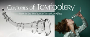 Banner for the "Centuries of Tomfoolery" exhibit. The banner is split into two sections. The larger section on the right side of the banner is an image of a clear horn-shaped trick glass in front of a white to gray gradient background. The background starts white at the bottom and turns darker towards the top of the image. The glass has six clear glass rings with small swirls in groups of two throughout the horn, a small knob at the tip, and a thick rim around the opening. The smaller section on the right side of the banner is an image of a lady with a clear horn-shaped trick glass in front of a dark teal background. The lady has her head tilted back as she pours a clear liquid out of the trick glass into her mouth. The liquid instead spills all over her face ,mouth, and light teal colored shirt. The lady has shoulder length, curly brown hair and red lipstick. Large white text extends across the top of the banner and reads "Centuries of Tomfoolery". Underneath is a teal rectangle that gets more transparent towards the left side of the banner. Inside of this rectangle is more white text that reads "Trick Glasses", "Pipes", and "Whimsical Delights".