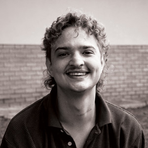 Grayscale portrait photo of Francois Pietersen. Francois has curly hair that stops under the ears, is wearing a dark shirt, and is smiling at the camera.