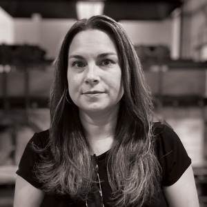 Grayscale portrait photo of Rebecca Arday. Rebecca is facing the camera, has long dark hair, and is wearing a dark short sleeve shirt.